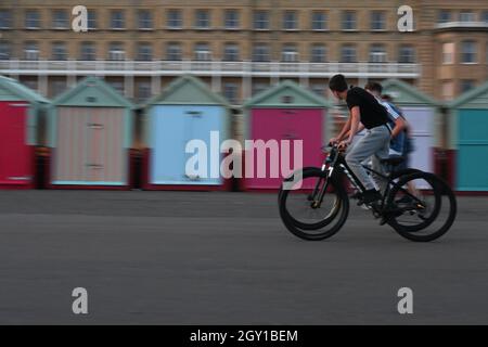 Two boys riding along Brighton Seafront with Beach Huts in the background, Stock Photo