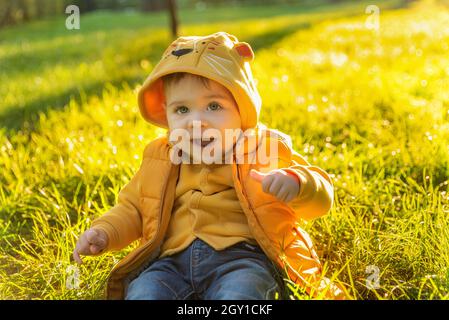 Emotive portrait of a smiling toddler boy. Happy Caucasian baby kid wearing yellow jacket against light green background outdoor at sunset Stock Photo
