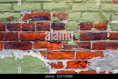 Painted green facade peels to show bright red brick underneath background Stock Photo