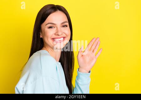 Photo of cute brown hairdo millennial lady wave arm wear blue hoodie isolated on yellow color background Stock Photo