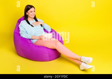 Full length body size photo girl laying in beanbag watching movie eating pop corn isolated vibrant yellow color background Stock Photo