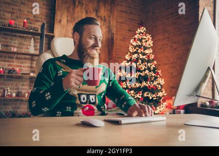 Photo of cheerful relaxed bearded ginger man sit desk hold coffee mug work wear sweater decorated office indoors Stock Photo