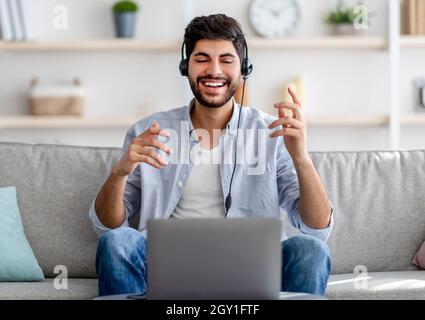 Distant communication concept. Happy millennial arab guy in headset talking and gesturing to laptop camera Stock Photo