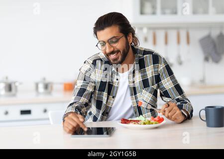 Positive arab guy having breakfast, using digital tablet, copy space Stock Photo