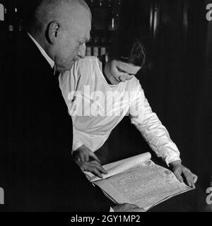 Ein Apotheker und seine Mitarbeiterin lesen das Faksimile eines alten Dokument von König Friedrich Wilhelm, Deutschland 1930er Jahre. A pharmacist and his female staff member reading a facsimile of an old document of Prussian king Frederick William, Germany 1930s. Stock Photo