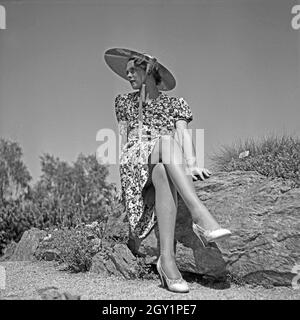 Eine junge Frau sitzt in einem Sommerkleid auf einem Felsen, Deutschland 1930er Jahre. A young woman wearing a summer dress sitting on a rock, Deutschland 1930s. Stock Photo