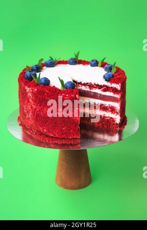 Sliced Birthday cake on the wooden cake stand. Red velvet cake decorated with mint leaves and blueberries. Green background. Copy space. Food photogra Stock Photo