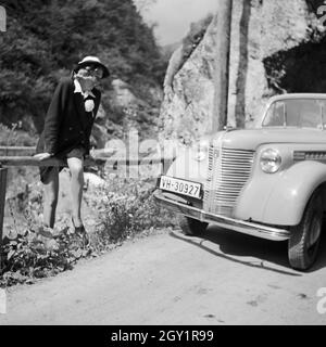 Eine Frau sitzt auf einem Geländer vor ihrem Opel Olympia in der Wachau in Österreich, Deutschland 1930er Jahre. A woman sitting on a railling in front of her Opel model Olympia at the Wachau area in Austria, Germany 1930s. Stock Photo
