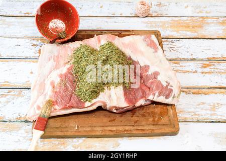 Preparation of a porchetta with a mixture of aromatic herbs placed on a piece of fresh pork belly open in the thickness Stock Photo