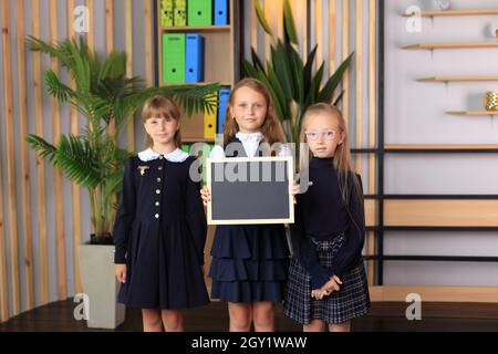 Three girls are holding a drawing board in a frame. Children holding a frame in their hands. Schoolgirls hold a blackboard with chalk. Stock Photo