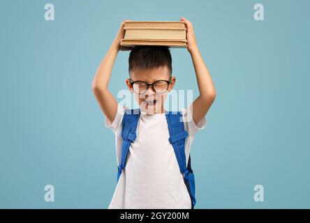 School Stress. Angry Asian Schoolboy Holding Books On Head And Shouting Stock Photo