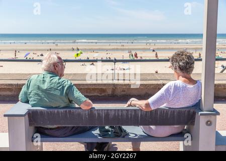 Two seniors sitting on a bench facing the beach Stock Photo