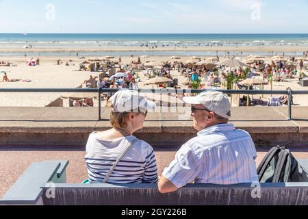 Two seniors sitting on a bench facing the beach Stock Photo