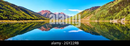 Panorama of lake in the mountains surrounded by fall trees and red sandy mountain peaks Stock Photo