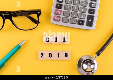 Yellow surface with glasses, a calculator, a stethoscope, a pen, and a 'GOA 2019' sign Stock Photo