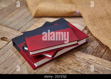 Three small red and black journals laying next to burlap cloth on a wooden surface Stock Photo
