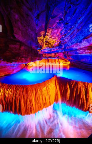 Large colorful underground waterfall in cave with orange and blue lights Stock Photo