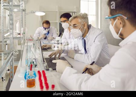 Group of scientist in protective respiratory mask working at laboratory Stock Photo