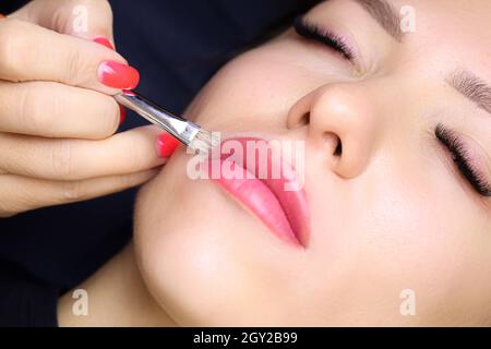 the tattoo artist holds a brush in his hand and smears a foundation near his lips correcting the finished tattoo work Stock Photo