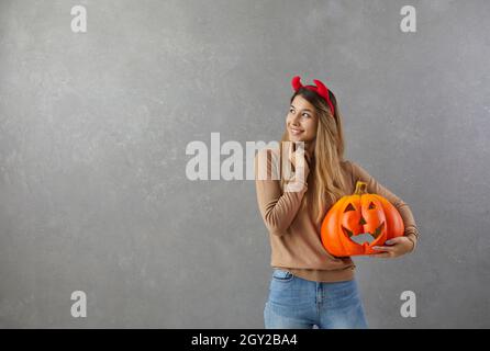 Happy woman standing on copy space background, holding pumpkin and thinking about Halloween party Stock Photo