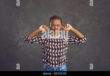 Capricious young African American woman covers her ears with her fingers so as not to hear anything. Stock Photo