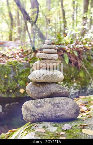 Serene stack of oval shaped rocks with trees and a river in the background Stock Photo