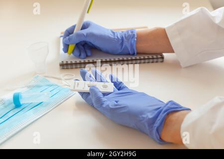 sars covid antigen test. doctor hands in blue gloves holding rapid test and writing results to note Stock Photo