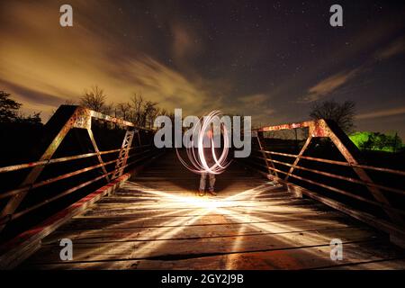 White swirling light on a metal bridge with light streaking across the bridge itself at dusk Stock Photo