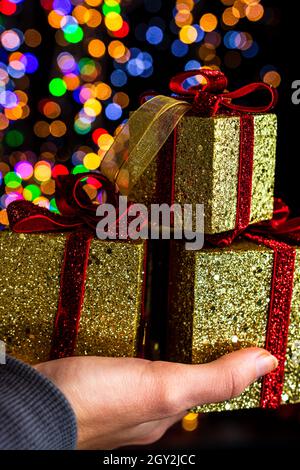 Vertical closeup shot of a hand holding decorated boxes with Christmas gifts on a bokeh background Stock Photo