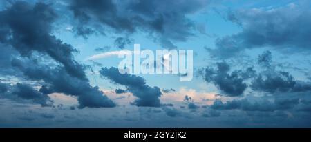 Blue stormy clouds blown by the strong wind across the sky at evening. Dramatic sky with torn dark clouds low over the horizon. Wide overcast skyscape Stock Photo