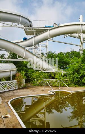 Brown water pool with a massive water slide in the background in an abandoned theme park Stock Photo