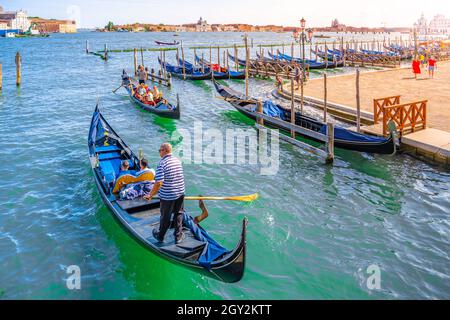 VENICE, ITALY - AUGUST 02, 2021: Tourists and gondolier on gondola boat. Romantic gondola cruise in Venetian water canal, Venice, Italy. Stock Photo