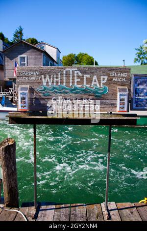 Old sign saying Whitecap Charters stands on a dock in front of a green and white river Stock Photo
