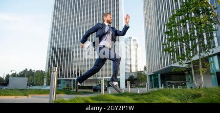 successful man in formalwear jumping with computer outside the office, technology Stock Photo