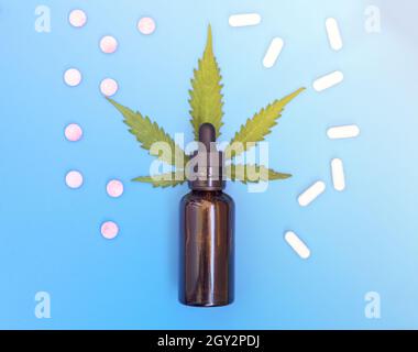 CBD pills. Group of CBD capsules and pink cannabidiol pills and hemp leaves on blue background. Assorted medical cannabis products. Medical marijuana Stock Photo