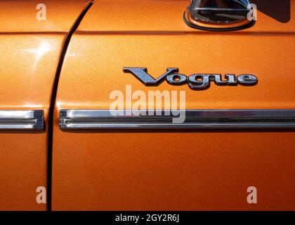 Image of the chrome badge on the side door of a Sunbeam Vogue car from the 1970s, the word Vogue above a chrome door strip on a metallic orange paint Stock Photo
