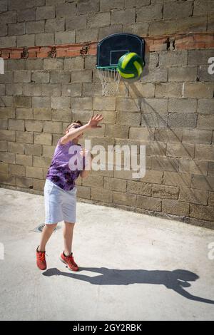 Vertical shot of a young caucasian male playing in the backyard near the basketball hoop Stock Photo