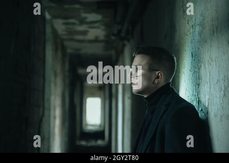 Young man with eyeglasses in dark ruined corridor Stock Photo