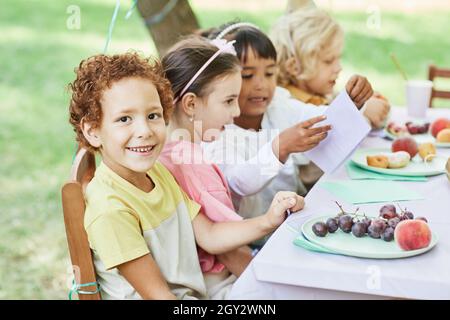 Portrait of smiling boy looking at camera at picnic table outdoors enjoying Birthday party with friends Stock Photo