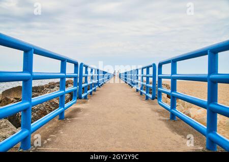 Cement walkway with colorful blue metal railing and walkers in distance Stock Photo