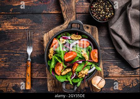 Healthy bistro green salad with mix leaves mangold, swiss chard, spinach, arugula and nuts in a pan. Dark wooden background. Top view Stock Photo