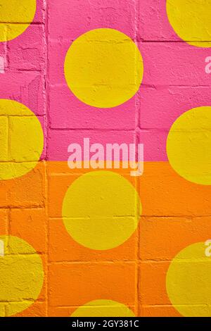 Vertical of cement wall up close divided by pink and orange paint with circles of yellow Stock Photo