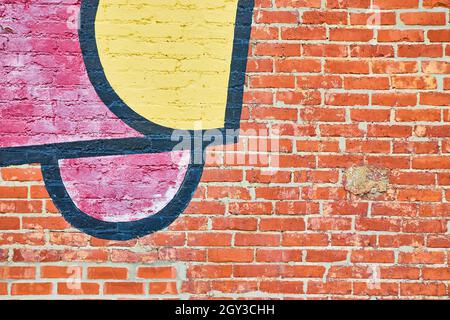 Wall of textured red brick up close with patch of red, black, and yellow graffiti Stock Photo