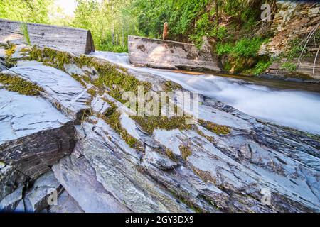 Stone jutting out of river with detail of moss and cement dam in background Stock Photo