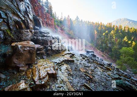 View behind waterfall with wet slippery rocks overlooking mountain in distance Stock Photo