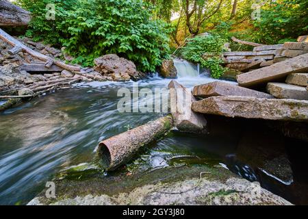 Metal rusted pipe in river with rubble and cement blocks by small waterfall Stock Photo