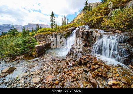 Beautiful waterfalls over tiers of gray and brown rocks with view of open valley and mountains Stock Photo