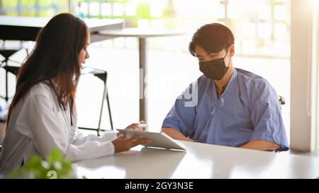 A professional specialist female doctor explains the abdomen system to a young male patient in the examination room using a digital tablet. Stock Photo