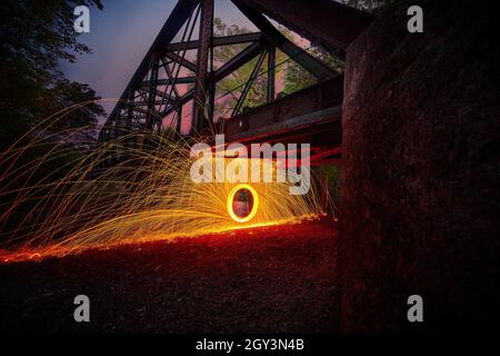 Spiral of steel wool orange sparks underneath large metal bridge Stock Photo