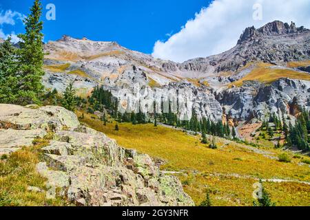 Lichen-covered rocks with view of beautiful mountain range covered in grey rocks and pine trees Stock Photo